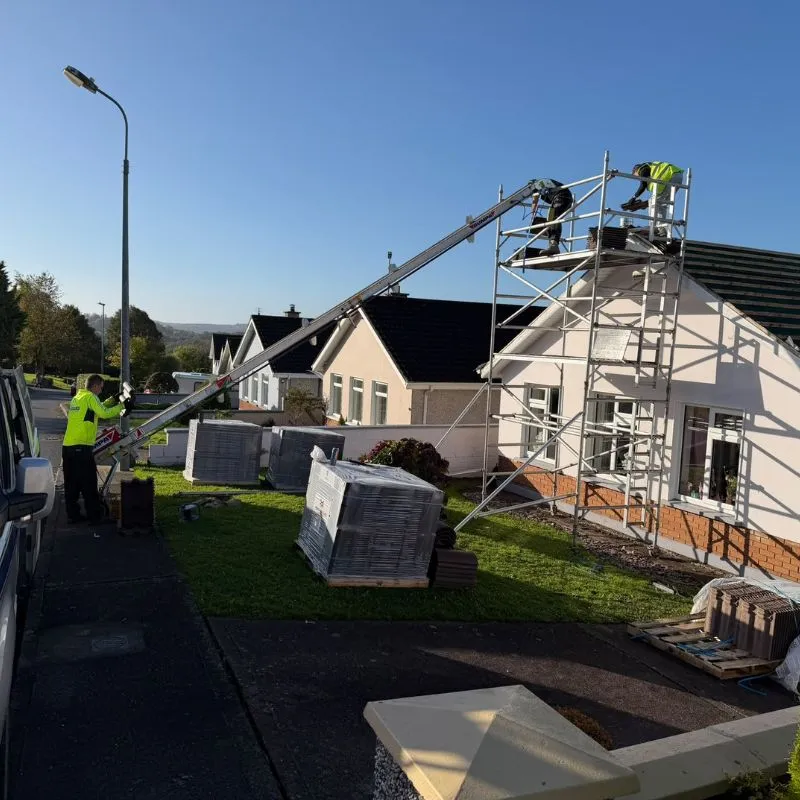 Roofers using a materials hoist beside scaffolding to lift roof tiles onto a house