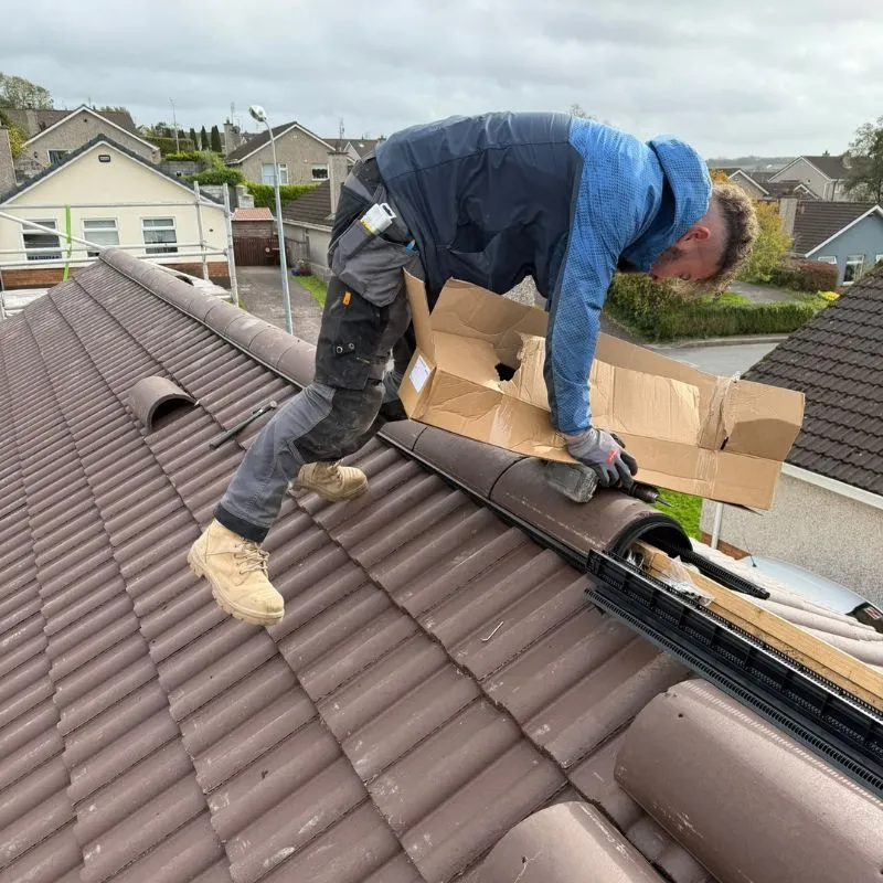 Roofer fitting half-round ridge tiles at the top of the tiled roof