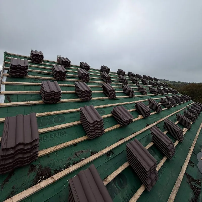 Stacks of brown roof tiles arranged on battens above green roofing underlay